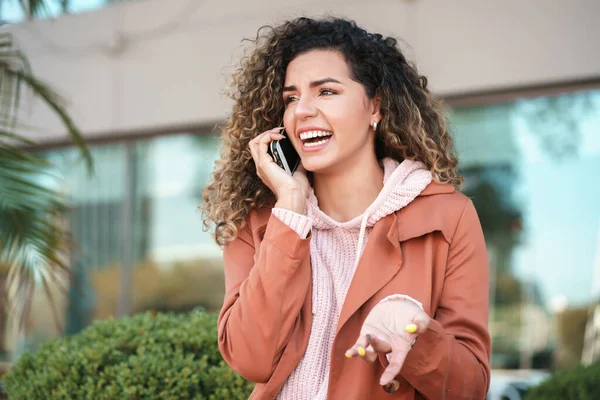 Latin woman smiling while talking on the phone outdoors in the street.