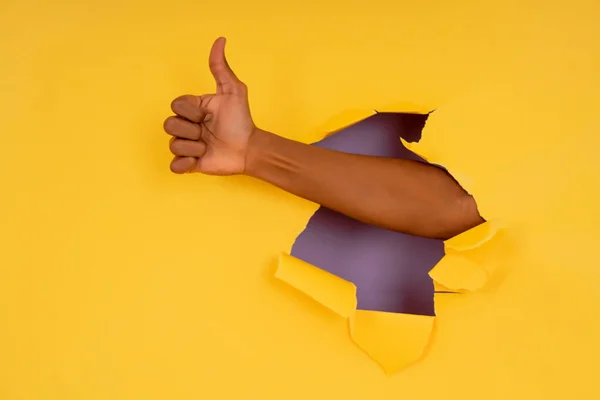 Main faisant geste pouce vers le haut avec la main à travers le mur de papier déchiré. — Photo