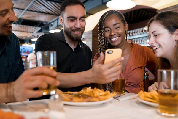 Grupo de amigos usando um telefone celular em um restaurante. — Fotografia de Stock