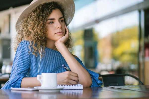 Femme avec une expression réfléchie sur son visage tout en écrivant sur un carnet. — Photo