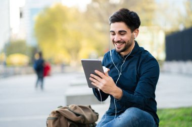 Genç adam dışarıda dijital tabletle video görüşmesi yapıyor..