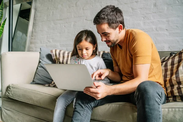 Liten flicka och hennes far använder en laptop tillsammans hemma. Stockbild