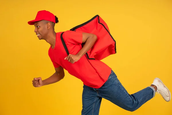 Giovane uomo di consegna in uniforme rossa che corre su sfondo isolato. Fotografia Stock