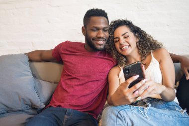 Çift evdeki koltukta otururken cep telefonu kullanıyor..