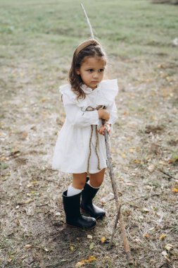 Beyaz bir elbise giymiş, kırsal kesimdeki çayırlarda dallarla oynayan sevimli küçük bir kız. 