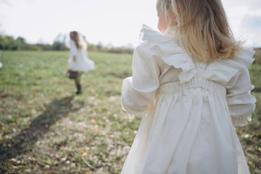 Kırsal kesimde çayır üzerinde oynayan beyaz, eski moda elbiseler giymiş güzel küçük kızlar. 