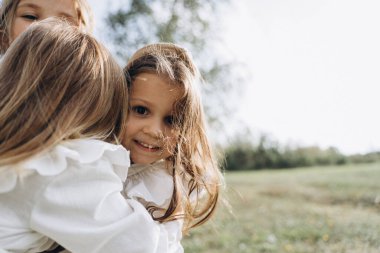 Beyaz elbiseli güzel küçük kızlar kırsalda birbirlerine sarılıyorlar.  