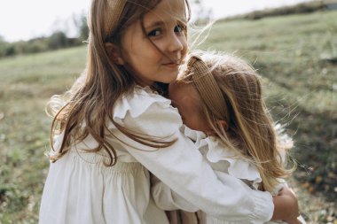 Beyaz elbiseli güzel küçük kızlar kırsalda birbirlerine sarılıyorlar.  