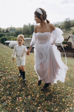 Beyaz bohem elbiseli güzel bir kadın. Çocuklarıyla kırsalda yürüyor. 