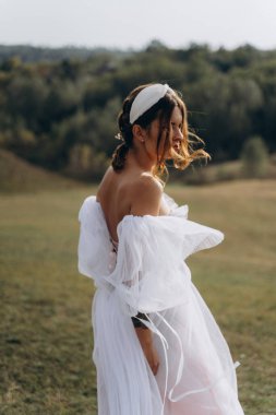Beyaz bohem elbiseli güzel bir kadın çayırda yürüyor ve kameraya poz veriyor. 