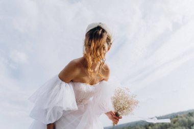 Beyaz bohem elbiseli güzel bir kadın çayırda yürüyor ve kameraya poz veriyor. 