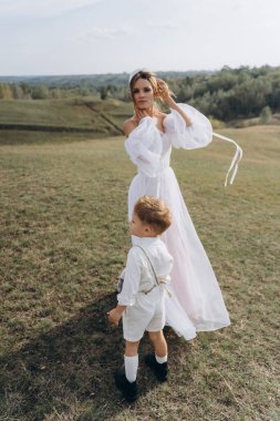 Beyaz bohem elbiseli güzel bir kadın. Çocuklarıyla kırsalda yürüyor. 