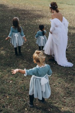 Beyaz bohem elbiseli güzel bir kadın çocuklarıyla kırsalda yürüyor. 