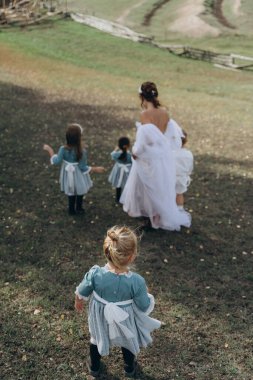 Beyaz bohem elbiseli güzel bir kadın çocuklarıyla kırsalda yürüyor. 