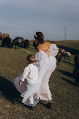 Beyaz bohem elbiseli güzel bir kadın. Çocuklarıyla kırsalda yürüyor. 