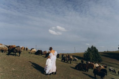 Beyaz bohem elbiseli güzel bir kadın. Çocuklarıyla kırsalda yürüyor. 