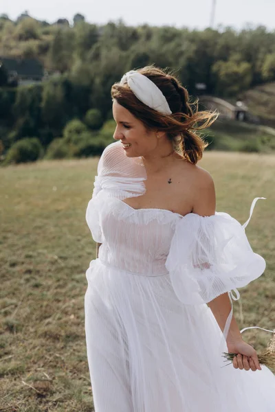 Beyaz bohem elbiseli güzel bir kadın çayırda yürüyor ve kameraya poz veriyor. 