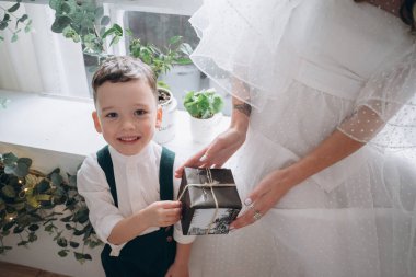 Çocuğuyla birlikte beyaz bir bohem elbise giymiş güzel bir kadın Noel süsleri olan bir odada ve oğlu annesine bir hediye veriyor. 