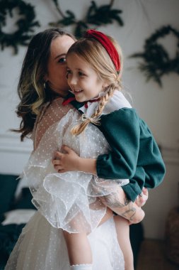 Beyaz bohem elbisesi giymiş güzel bir kadın Noel süslemeleri olan bir odada küçük kızıyla kibarca iletişim kuruyor.