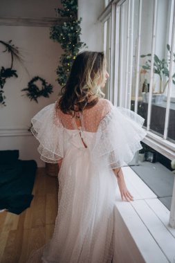 Noel arifesinde pencerenin yanında bohem beyaz elbise giymiş güzel bir kadın.