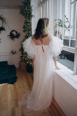 Noel arifesinde pencerenin yanında bohem beyaz elbise giymiş güzel bir kadın.