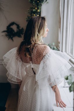 Noel arifesinde pencerenin yanında bohem beyaz elbise giymiş güzel bir kadın.