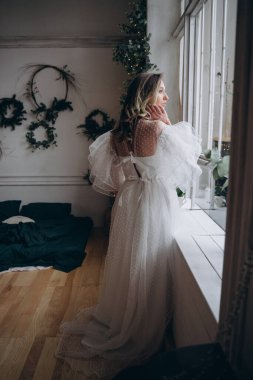 Noel arifesinde pencerenin yanında bohem beyaz elbise giymiş güzel bir kadın.