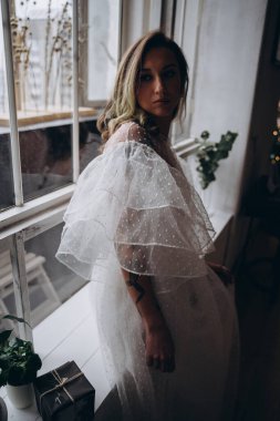Noel arifesinde pencerenin yanında bohem beyaz elbise giymiş güzel bir kadın.