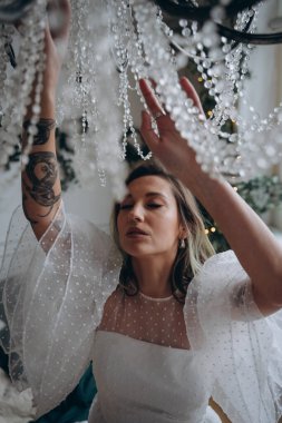 Bohem beyaz elbiseli güzel bir kadın avizeyi siliyor.  