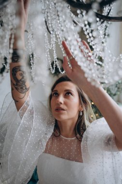 Bohem beyaz elbiseli güzel bir kadın avizeyi siliyor.  