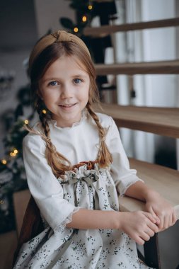 Noel arifesinde bohem beyaz çiçekli elbise giymiş güzel bir kız merdivenlerde oturuyor.