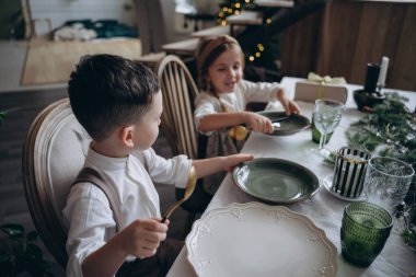 Noel masasında oturan şenlikli elbiseli güzel çocuklar