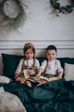 Bohem gibi giyinmiş güzel çocuklar kanepede oturup Noel süsleriyle dolu bir odada kitap okuyorlar.