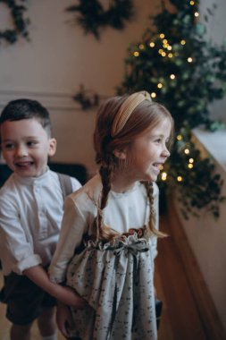 Kardeşiyle bohem elbiseler giymiş güzel bir kız Noel süsleriyle dolu bir odada oynuyor.