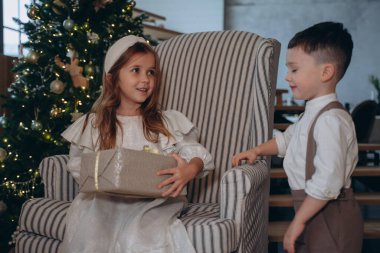 Bohem beyaz elbiseler giymiş güzel bir kız. Kardeşi sandalyede oturuyor ve Noel ağacının önünde hediyeleri açıyor.