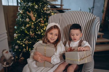 Bohem beyaz elbiseler giymiş güzel bir kız. Kardeşi sandalyede oturuyor ve Noel ağacının önünde hediyeleri açıyor.