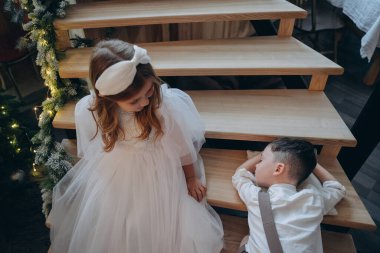 Erkek kardeşi tahta merdivenlerde otururken ve küçük çocuk da basamaklarda uyurken bohem beyaz elbiseler giymiş güzel bir kız.