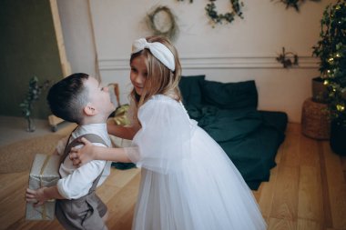 Erkek kardeşi Noel ağacının yanında bohem beyaz elbiseli güzel bir kız ve kız kardeşinden bir hediye saklayan bir oğlan.