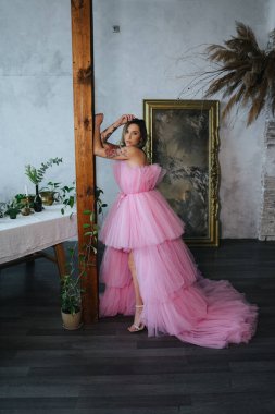 Peçeli, yeni pembe elbiseli güzel bir kadın resmin önünde duruyor ve kameraya poz veriyor.