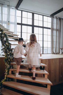 Erkek kardeşi pencerenin arkasındaki ahşap merdivenleri çıkarken beyaz bir elbise giymiş güzel bir kız.