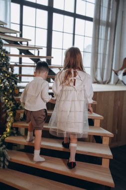 Erkek kardeşi pencerenin arkasındaki ahşap merdivenleri çıkarken beyaz bir elbise giymiş güzel bir kız.