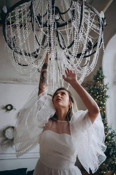 Bohem beyaz elbiseli güzel bir kadın avizeyi siliyor.  