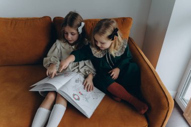 Bohem elbiseler giymiş güzel kızlar Noel arifesinde kanepede oturup pencerenin yanında kitap okuyorlar.