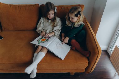 Bohem elbiseler giymiş güzel kızlar Noel arifesinde kanepede oturup pencerenin yanında kitap okuyorlar.