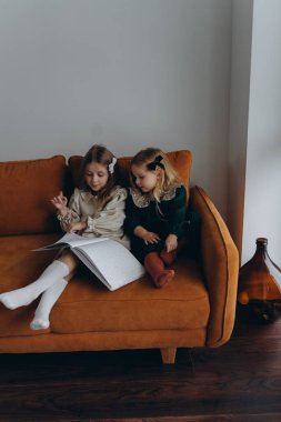 Bohem elbiseler giymiş güzel kızlar Noel arifesinde kanepede oturup pencerenin yanında kitap okuyorlar.
