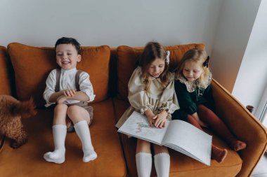 Bohem gibi giyinmiş güzel çocuklar Noel arifesinde kanepede oturup pencerenin yanında kitap okuyorlar.