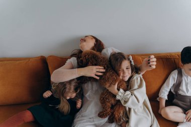 Beyaz bohem bir elbise giymiş güzel kızıl saçlı kadın küçük kızları ve oğluyla birlikte Noel arifesinde kanepede oturuyor. 