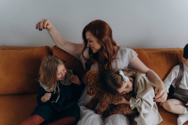 Beyaz bohem bir elbise giymiş güzel kızıl saçlı kadın küçük kızları ve oğluyla birlikte Noel arifesinde kanepede oturuyor. 