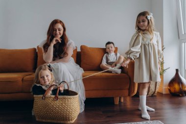 Kızları ve oğluyla birlikte beyaz bohem elbiseler giymiş güzel bir kızıl kadın Noel arifesinde birlikte vakit geçiriyorlar ve en küçük kız sepette oturuyor.