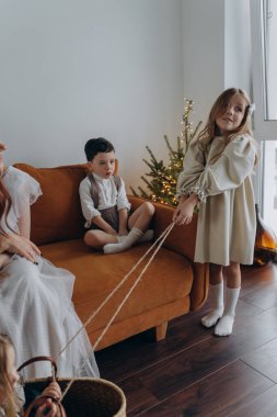 Kızları ve oğluyla birlikte beyaz bohem elbiseler giymiş güzel bir kızıl kadın Noel arifesinde birlikte vakit geçiriyorlar ve en küçük kız sepette oturuyor.